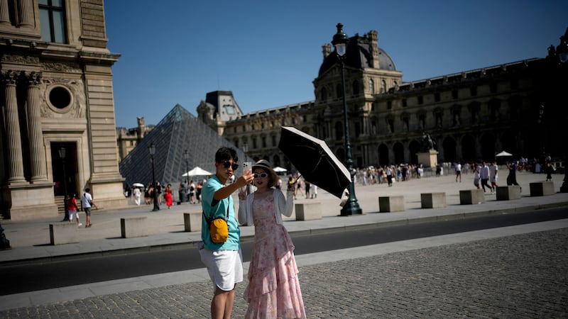 Turistas con un paraguas se toman una foto en París el lunes 22 de junio de 2026, en medio de...